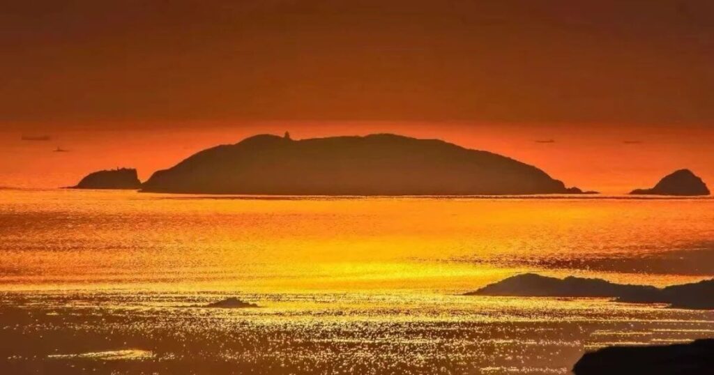 夕陽映照下的洛迦山，海面金光閃爍，遠處島嶼剪影清晰可見。